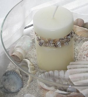 eine Glaschale mit Sand, Muscheln und einer hellen Kerze