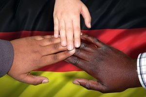 drei Hände aus verschiedenen Nationen berühren sich an den Fingerspitzen, darunter liegt eine Deutschlandfahne