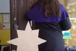 ein Sternsinger schreibt den Segen an, davor steht ein Kind mit Stern in der Hand