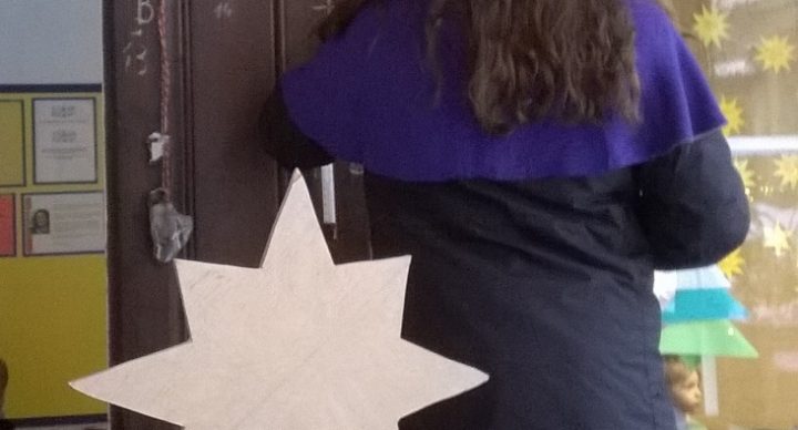 ein Sternsinger schreibt den Segen an, davor steht ein Kind mit Stern in der Hand